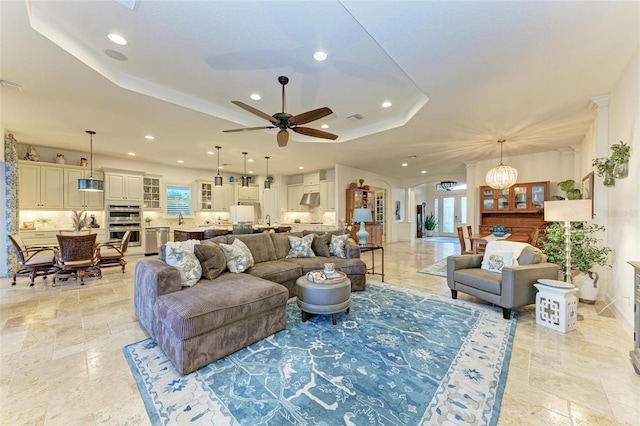 living room with ceiling fan with notable chandelier and a raised ceiling