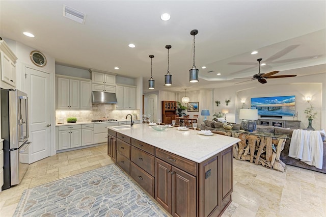 kitchen featuring sink, stainless steel appliances, decorative light fixtures, dark brown cabinets, and a center island with sink