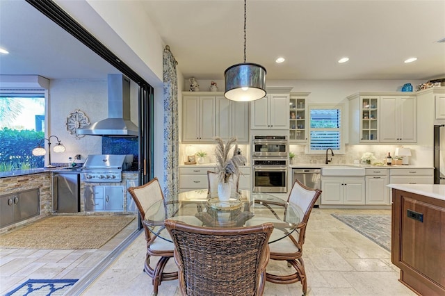 kitchen with sink, hanging light fixtures, wall chimney exhaust hood, tasteful backsplash, and stainless steel appliances