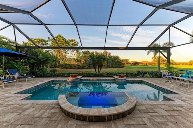 pool at dusk featuring a lanai, a patio area, and an in ground hot tub