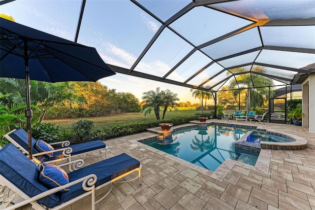 pool at dusk with glass enclosure, an in ground hot tub, and a patio