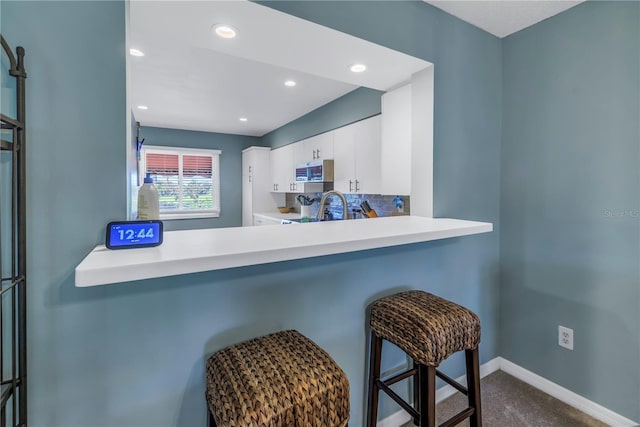 kitchen with a kitchen bar, kitchen peninsula, tasteful backsplash, and white cabinetry