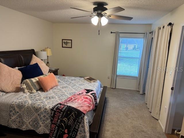 carpeted bedroom featuring ceiling fan and a textured ceiling