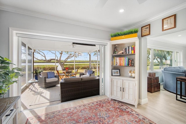 living area featuring built in shelves, light hardwood / wood-style floors, ceiling fan, and ornamental molding