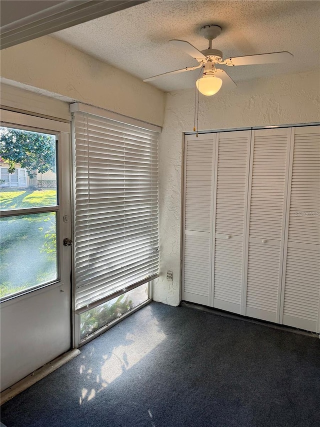 unfurnished bedroom featuring dark colored carpet, a textured ceiling, and ceiling fan