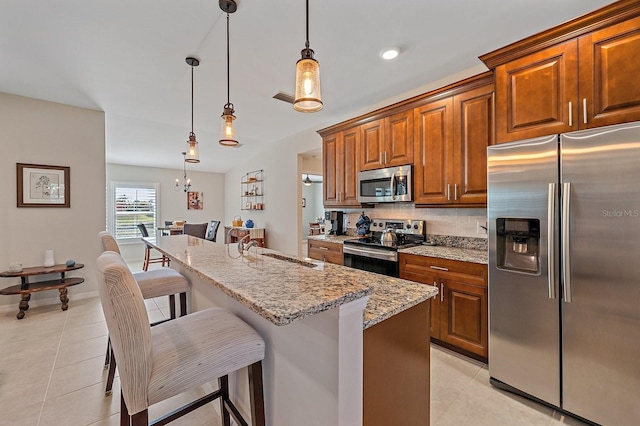 kitchen with a kitchen bar, appliances with stainless steel finishes, a kitchen island with sink, sink, and pendant lighting