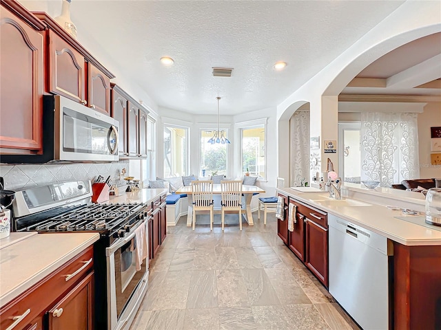 kitchen featuring sink, stainless steel appliances, pendant lighting, a textured ceiling, and decorative backsplash