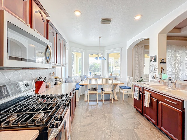 kitchen featuring backsplash, a textured ceiling, decorative light fixtures, stainless steel appliances, and a chandelier