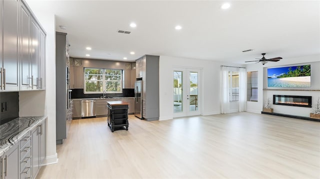 kitchen with visible vents, open floor plan, appliances with stainless steel finishes, decorative backsplash, and a glass covered fireplace