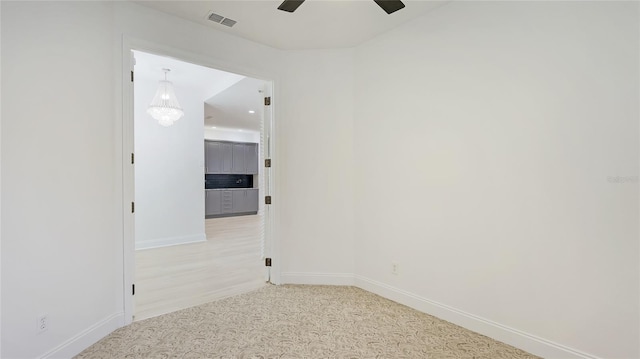 carpeted empty room with baseboards, visible vents, and a ceiling fan