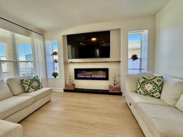 living area with a glass covered fireplace, baseboards, and wood finished floors