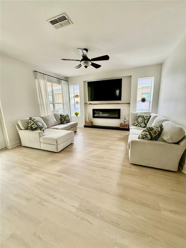 living area with light wood finished floors, plenty of natural light, visible vents, and a glass covered fireplace