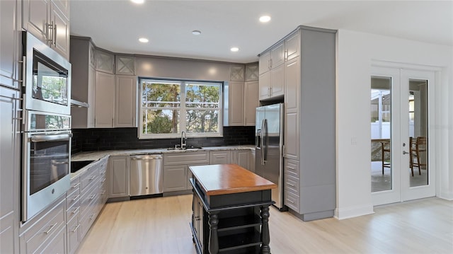 kitchen featuring tasteful backsplash, stainless steel appliances, a sink, and gray cabinetry