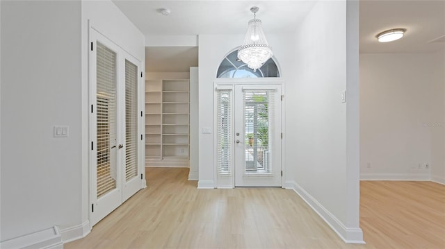 entrance foyer with light wood-type flooring, baseboards, a chandelier, and french doors