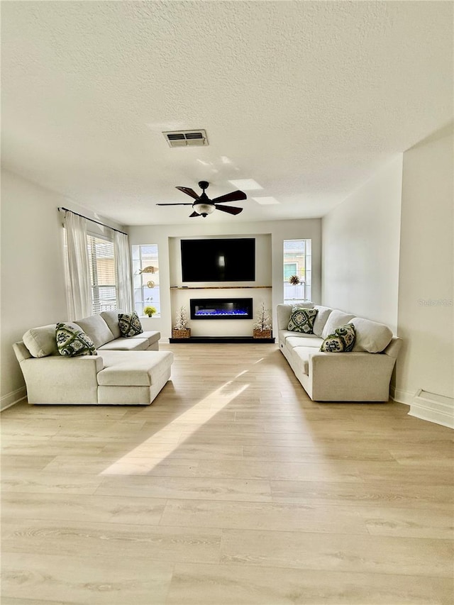 living room featuring ceiling fan, wood finished floors, visible vents, and a healthy amount of sunlight