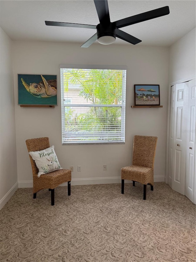 living area featuring carpet, baseboards, and ceiling fan