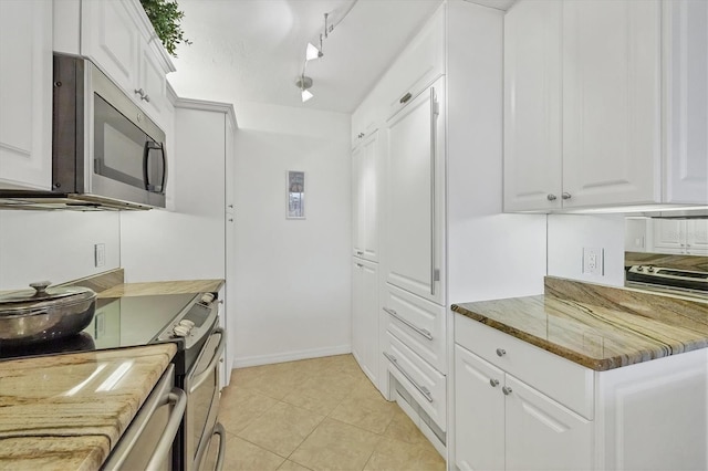 kitchen with stone counters, track lighting, white cabinets, light tile patterned floors, and stainless steel appliances