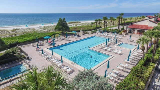 view of pool featuring a patio area, a water view, and a beach view