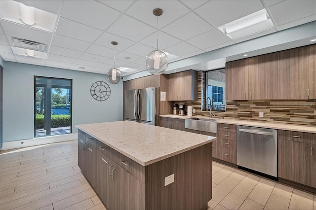 kitchen with sink, stainless steel appliances, backsplash, decorative light fixtures, and a kitchen island