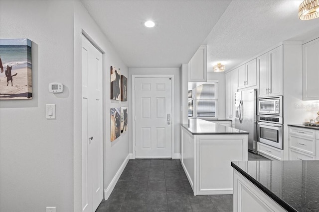 kitchen with kitchen peninsula, appliances with stainless steel finishes, white cabinetry, and dark stone counters