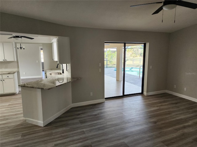 kitchen with kitchen peninsula, light stone countertops, dark wood-type flooring, sink, and white cabinetry