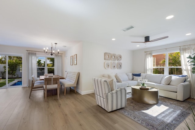 living room featuring ceiling fan with notable chandelier, plenty of natural light, and light hardwood / wood-style flooring