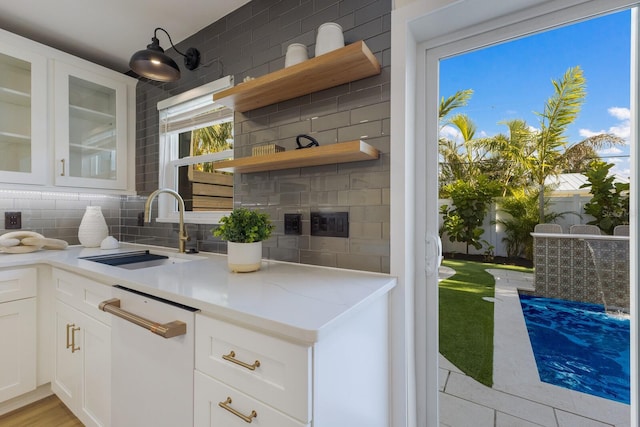 kitchen with dishwasher, backsplash, sink, light stone counters, and white cabinetry