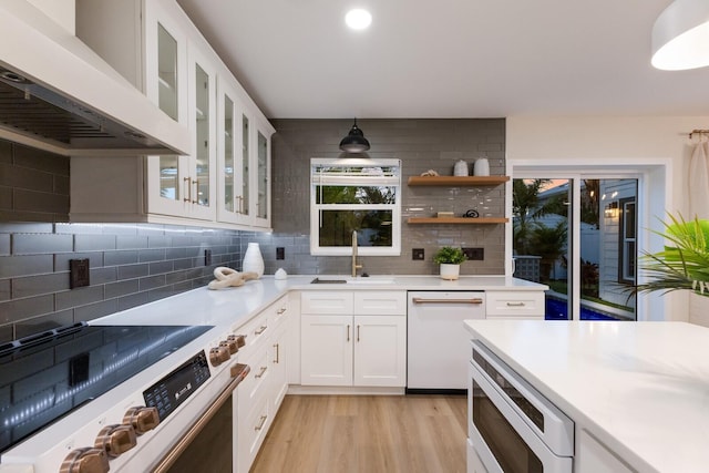 kitchen with stove, white dishwasher, sink, custom range hood, and white cabinetry