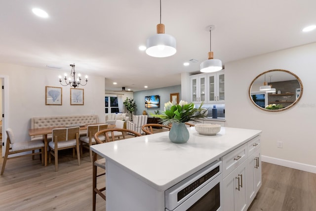 kitchen with a center island, stainless steel microwave, decorative light fixtures, light hardwood / wood-style floors, and white cabinetry