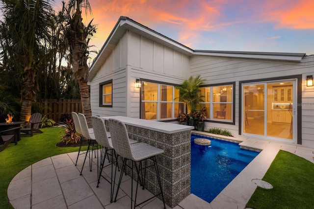 back house at dusk featuring a lawn, a fenced in pool, an outdoor bar, and a patio