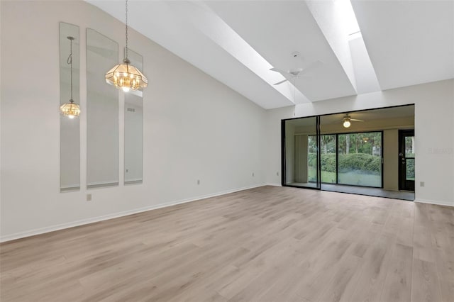 unfurnished living room featuring lofted ceiling with skylight, ceiling fan with notable chandelier, and light wood-type flooring