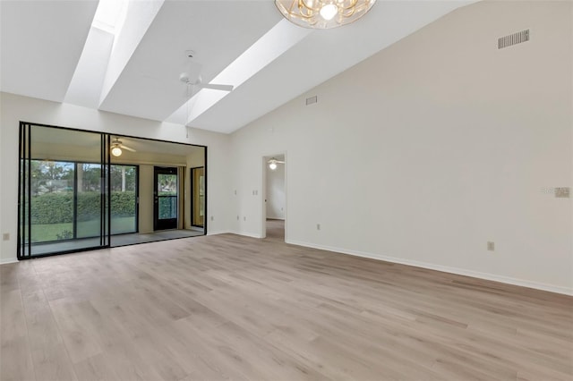 unfurnished room with a skylight, high vaulted ceiling, ceiling fan with notable chandelier, and light wood-type flooring