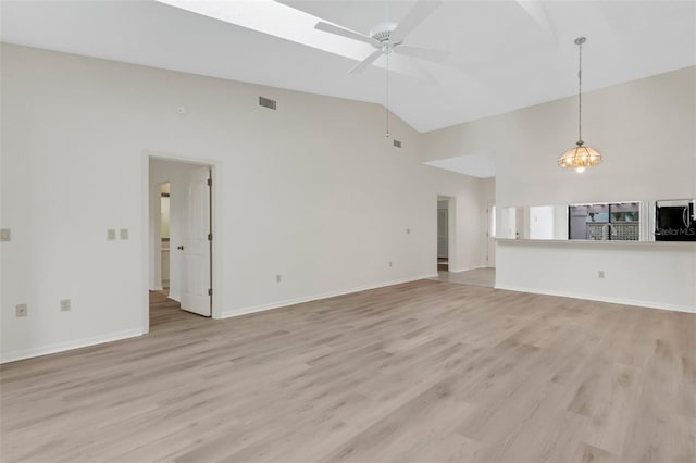 unfurnished living room with ceiling fan with notable chandelier, light hardwood / wood-style floors, and lofted ceiling with skylight