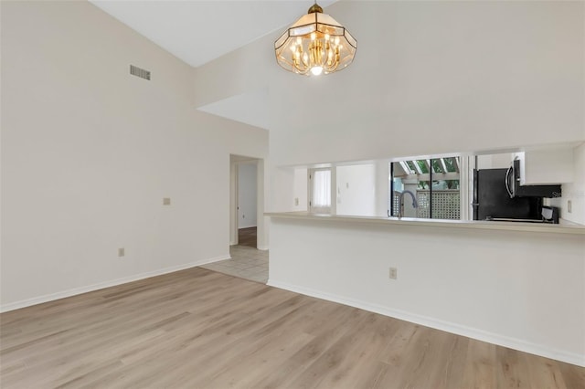 unfurnished living room with vaulted ceiling, light hardwood / wood-style floors, an inviting chandelier, and sink