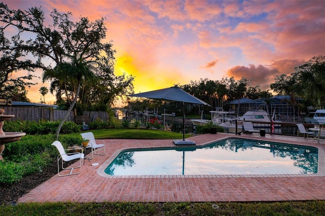 pool at dusk with a patio area, fence, and a fenced in pool