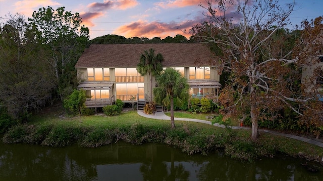 back house at dusk with a water view and a balcony