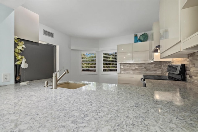 kitchen with a wood stove, light stone countertops, sink, stainless steel range with electric stovetop, and decorative backsplash