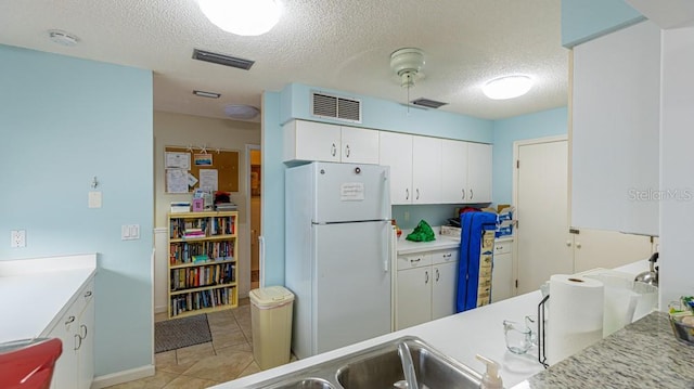 kitchen with white cabinets, a textured ceiling, white refrigerator, and light tile patterned floors