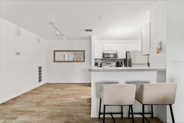 kitchen with white cabinetry, a kitchen breakfast bar, tasteful backsplash, kitchen peninsula, and appliances with stainless steel finishes