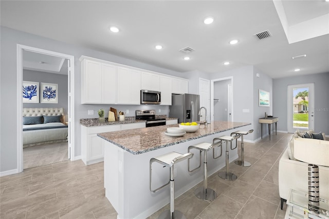 kitchen with a kitchen breakfast bar, white cabinetry, a center island with sink, and appliances with stainless steel finishes