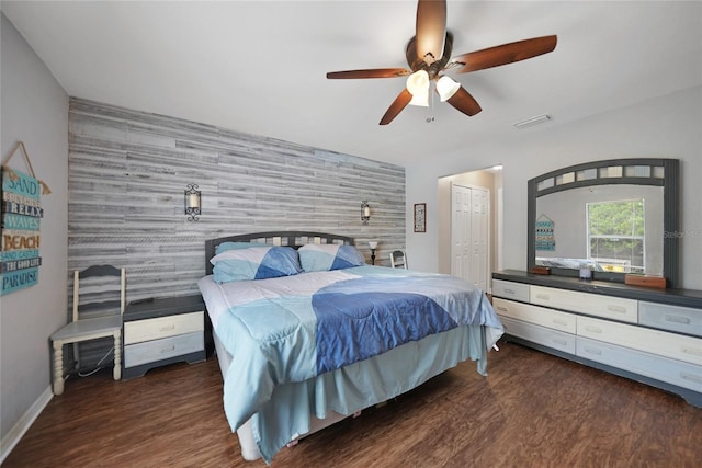 bedroom featuring ceiling fan, wood walls, dark wood-type flooring, and a closet