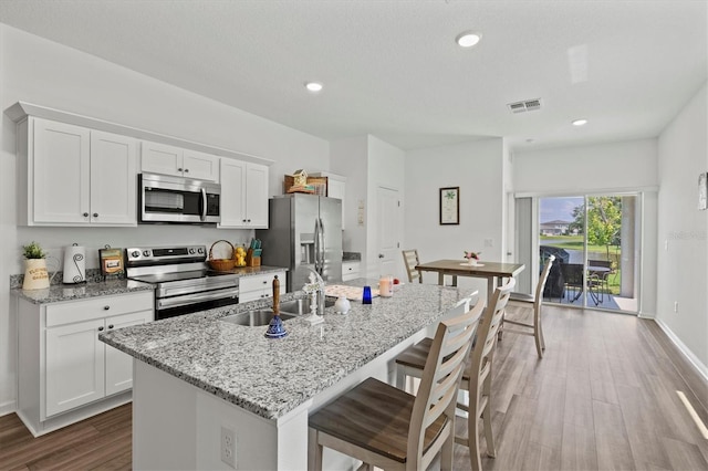 kitchen with a kitchen island with sink, white cabinets, light stone countertops, and appliances with stainless steel finishes