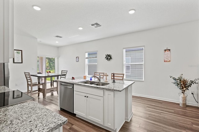 kitchen with light stone counters, stainless steel dishwasher, sink, a center island with sink, and white cabinets