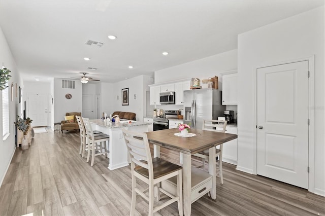 kitchen featuring a kitchen island with sink, a kitchen breakfast bar, ceiling fan, white cabinetry, and stainless steel appliances