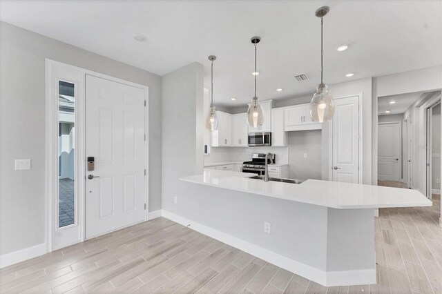 kitchen featuring sink, hanging light fixtures, kitchen peninsula, white cabinets, and appliances with stainless steel finishes