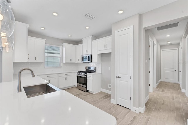 kitchen featuring white cabinets, sink, tasteful backsplash, light hardwood / wood-style floors, and stainless steel appliances