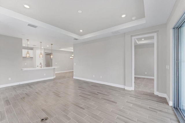 unfurnished living room featuring a raised ceiling and sink