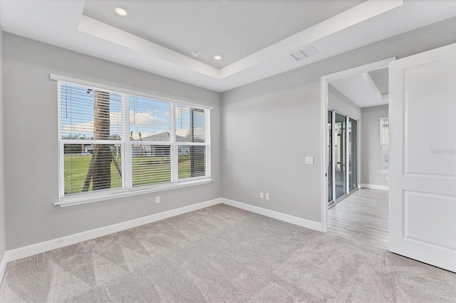 empty room with a raised ceiling and light carpet