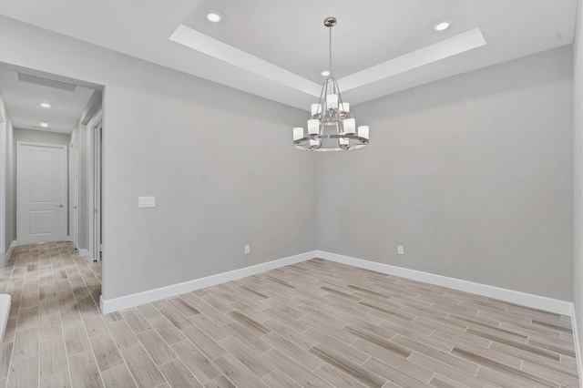 spare room with light wood-type flooring, a tray ceiling, and an inviting chandelier