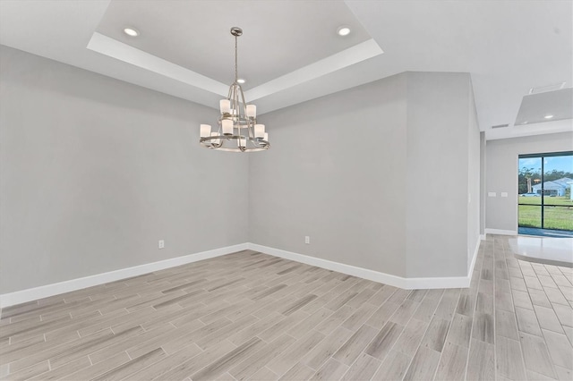 empty room with a chandelier, light hardwood / wood-style floors, and a raised ceiling